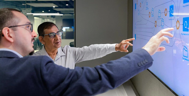 Two persons pointing at statistics on a big screen 