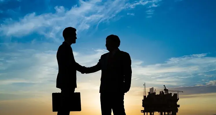 businessmen shaking hands amid oil and gas background